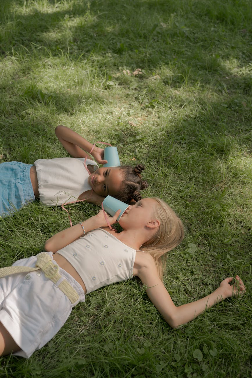 two girls laying on lawn and playing paper cups connected with string